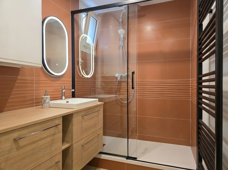 Salle de bains moderne avec douche à l'italienne, paroi en verre trempé, meuble vasque suspendu en bois clair avec tiroirs, robinet mitigeur chromé, miroir LED ovale lumineux encastré