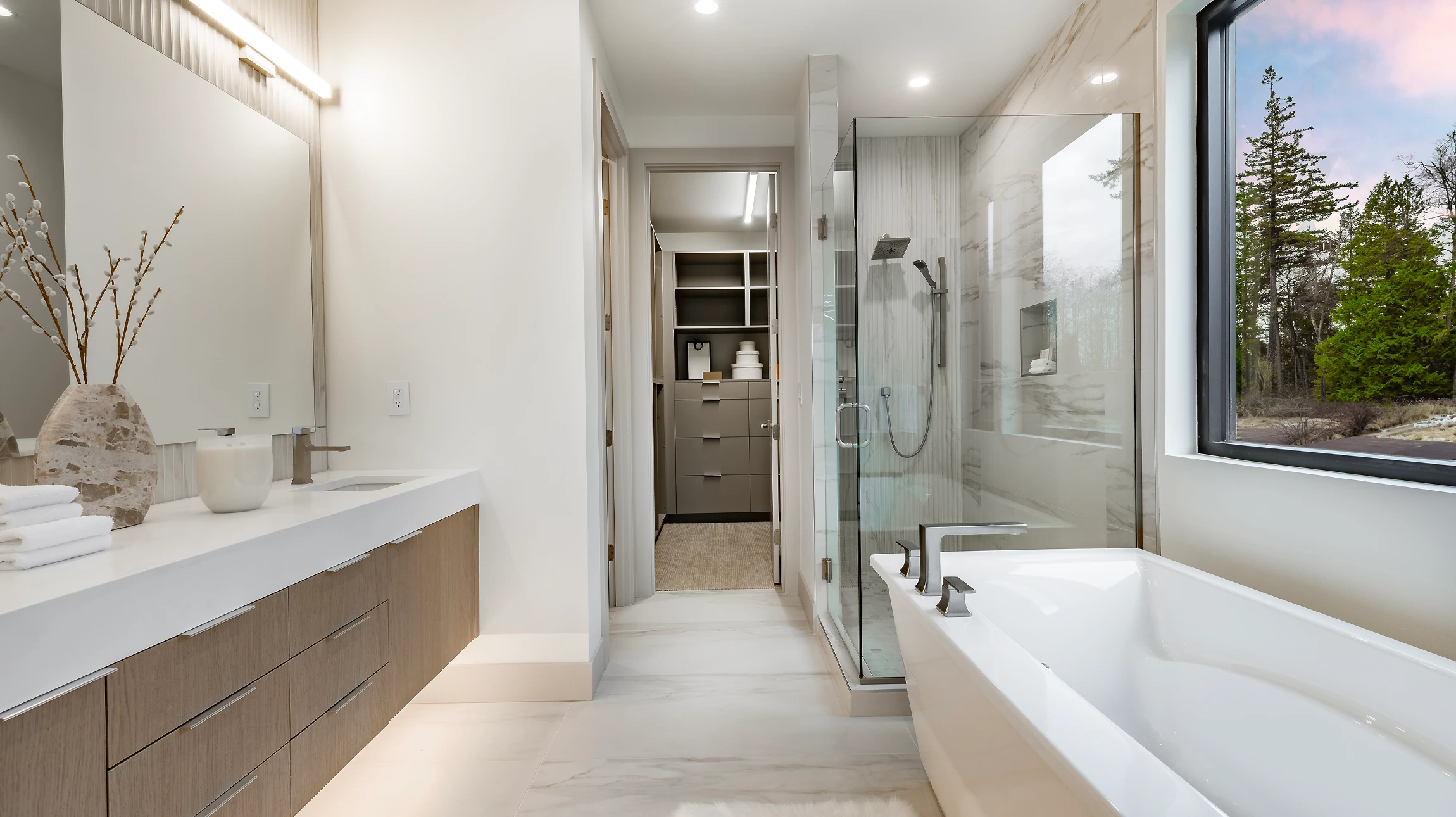 Salle de bain moderne luxueuse avec baignoire encastrée en marbre beige veiné, douche à l'italienne vitrée, carrelage grand format effet pierre naturelle