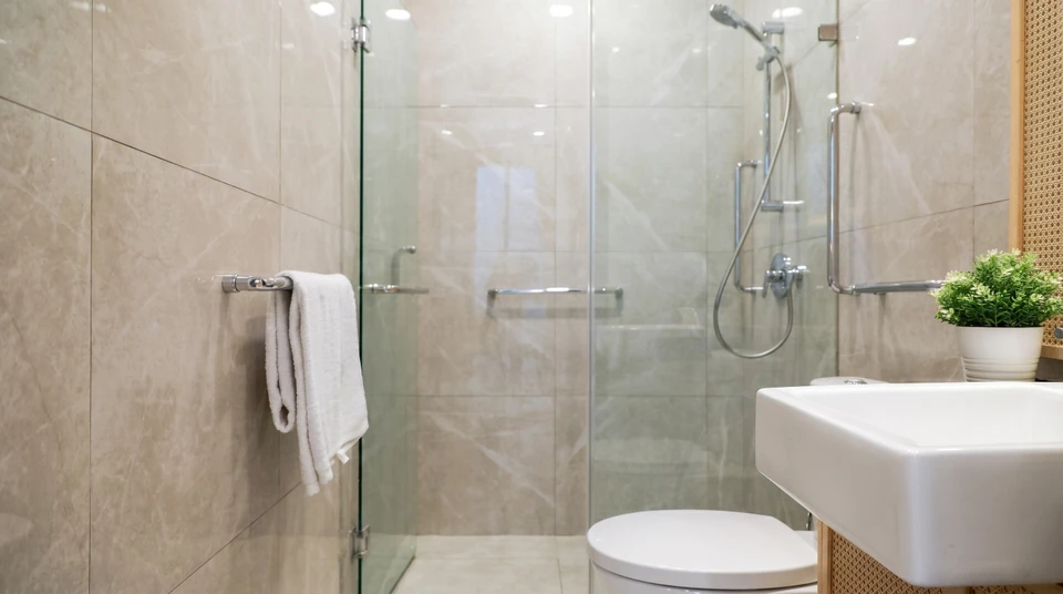 Un installateur professionnel en polo noir et ceinture à outils examine une paroi de douche vitrée dans une salle de bain moderne aux murs blancs