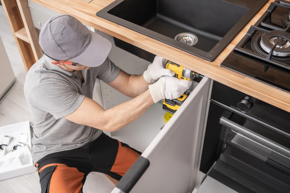 Cuisine moderne avec installateur professionnel en uniforme rouge montant un tiroir blanc dans meuble bas gris anthracite